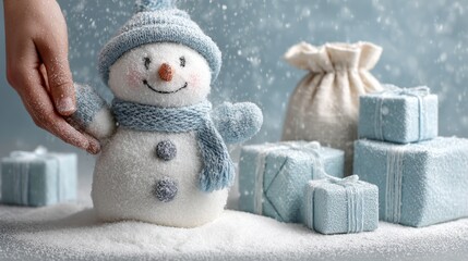 Wall Mural - a hand adjusts a small snowman adorned in a blue scarf and hat, surrounded by snow, blue gift boxes,