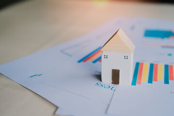 Poster - Small wooden house model on business documents with colorful graphs and charts illustrating real estate investment trends