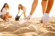 © maxbelchenko - A group of volunteers collect plastic bottles and trash on a sandy beach. Young men and women collect trash on the ocean shore, clean up the environment. The concept of ecology and volunteering.