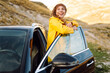 © maxbelchenko - Traveler in bright raincoat sits in car trunk and enjoys mountain landscape. Beautiful woman near car feels freedom on road. Nature, travel concept, road trip.