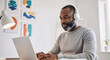 © Atmospheres - Focused African American man with headphones working remotely on a laptop in a stylish modern home office.