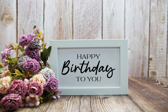 Happy Birthday To You text with flower decoration on wooden background