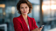 © Nataliya - Confident businesswoman in red jacket using smartphone in office