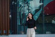 © Parichat - Smiling businesswoman walking and talking on cell phone outside modern office building