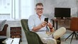 © nyul - Entrepreneur relaxing in comfortable chair, working in home office. Mid adult man using smartphone and wearing earbuds. Happy, confident middle age male smiling.