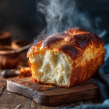 Aromatyczny bochenek świeżego, drożdżowego pieczywa, jeszcze parującego, leży na drewnianej desce do krojenia. Obok niego widać skrawek niebieskiej tkaniny.