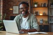 © Vadym - Smiling middle-aged African American man in glasses, wearing casual attire, works on laptop in home office. Mature businessman studies online, engaged in freelance work. Man smiles, focused on