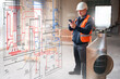 © Grispb - Construction engineer in safety vest and helmet using smartphone to check HVAC duct layout on site with schematic overlay. - Construction. Engineering. Ventilation.