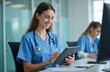 © Vadym - Young female nurse wearing blue scrubs, stethoscope works on digital tablet in modern clinic office. Medical pro uses technology for healthcare tasks, smiles. Another nurse visible in background.