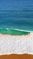 Poster - Aerial view of ocean wave washing onto a sandy beach with ripple sand textures, creating a serene and peaceful coastal scenery