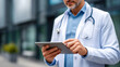 © INT888 - Doctor using tablet to access patient records outside modern medical facility, wearing white coat and stethoscope, focused on screen, professional healthcare environment, daytime lighting