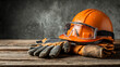 © Farukhassan - Orange hard hat and work gloves with safety goggles resting on a rustic wooden surface against a textured gray background