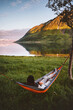 © EVERST - Weekend camping trip outdoor - man chilling in hammock travel lifestyle summer vacation in Norway, traveler enjoying tranquil sunset view of mountains and fjord harmony with nature sustainable tourism
