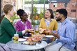 © sofiko14 - Group of friends enjoy pizza and drinks at an outdoor restaurant, laughing and talking.