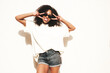 © halayalex - Beautiful woman with afro curls hairstyle.Smiling hipster model in white t-shirt. Sexy carefree female posing in the street near white wall in sunglasses. Cheerful and happy.Shaws peace sign