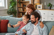 © Stockphotodirectors - A family smiles and shares laughter as they take a selfie together on the couch, showcasing a moment of joy and connection in their living room.