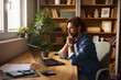 © Stockphotodirectors - A man sits at a wooden desk in a sunlit home office, deeply engaged with his laptop. Surrounding him are plants and books, creating a warm, inviting workspace.