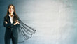 © Who is Danny - Confident businesswoman in suit with drawn superhero cape on textured wall background, symbolizing leadership, success, and empowerment concept.