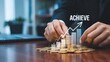 © PNG STOCK - Businessman stacking coins with a rising graph and the word achieve
