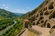 © The 2R Artificiality - Wide-angle shot of a cave monastic settlement overlooking a river valley and lush hills on a bright summer afternoon