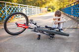 Little boy sitting on road hugging his knees next to fallen bicycle. Riding without helmet. Cycling safety precautions. Traffic accident with children. Bike safety for kids.