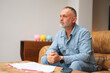 © Iryna - Man sitting on couch engaged in thought while reviewing documents in a cozy living room setting during the afternoon