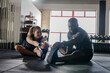 © Wavebreak Media - Diverse training partners sitting on rubber mats stretching toes near dumbbell rack in fitness gym