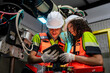 © VStudio - Two people wearing orange vests and white helmets are looking at a tablet. Team of engineers collaborating on programming and maintenance of a robotic arm in a smart factory.