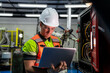© VStudio - A man wearing a green and orange vest is looking at a laptop. Electrical engineer or technician using a laptop for diagnostics and maintenance of a machine control panel in a factory.