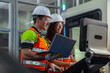 © VStudio - Two people wearing safety gear and holding a laptop. Team of engineers programming and operating a CNC machine in a smart factory.