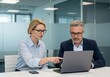 © shahida  - Focused business professionals collaborating on a laptop in a modern office environment discussing project details