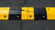© SEPTI - Damaged Black and Yellow Speed Bump on Asphalt Road with Visible Cracks in the Surface