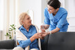 © New Africa - Nurse giving glass of water and pills to senior woman indoors. Home health care service