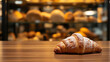 © Tameem - A single croissant, dusted with powdered sugar, sits on a dark wooden surface. The background is blurred, suggesting a warm, bakery setting. The focus is sharp on the pastry, highlighting its texture