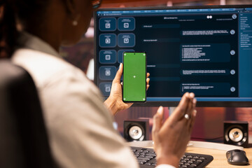 Poster - Woman seated at desk using AI LLM chatbot software and green screen phone in modern urban home office. Person uses large language model program on computer and mockup smartphone in apartment