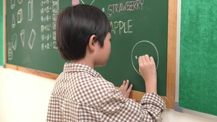 Poster - Asian boy drawing picture to express and develop imagination while standing at blackboard in classroom. Attractive elementary student writing at blackboard in art lesson. Education concept. Pedagogy.