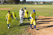 © Wavebreak Media - Diverse male baseball team with coach crossing infield at baseball park wearing uniforms, gloves