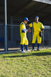 © Wavebreak Media - Baseball teammates in yellow jerseys leaning against chain-link fence on field gesturing with glove