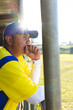 © Wavebreak Media - Sitting in dugout at chain-link fence, Hispanic man wearing yellow jersey, blue cap, copy space