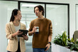 © Wavebreak Media - Asian coworkers walking and talking in office corridor holding tablet, coffee cup, smartphone