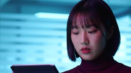 Poster - Focused Young Woman Using Tablet Device with Blue Background Lighting and Dark Turtleneck Top Indoors