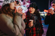 © qunica.com - Friends gathered at night enjoying warm cups of beverage, sharing joyful conversations and laughter together during the winter holiday season under festive lighting.