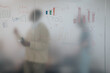 © qunica.com - Colleagues engage in creative brainstorming, analyzing charts and graphs on a frosted glass board during a project meeting. The atmosphere is collaborative and focused on team success.