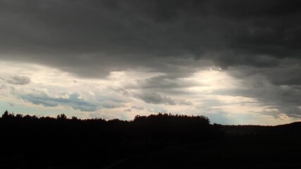 Wall Mural - timelapse of dramatic clouds with sun rays shining through. silhouette of swaying trees below. spect