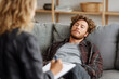 © stockmotion - Man lying on sofa during therapy session in office