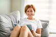 © Louis-Paul Photo - Portrait of smiling middle aged woman reading book at home