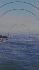 Poster - Concentric blue circles animation over ocean waves and rocky shoreline