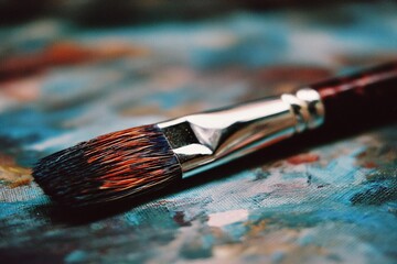 Poster - Close-up view of a paintbrush resting on a colorful canvas, highlighting vibrant paints and artistry in the studio