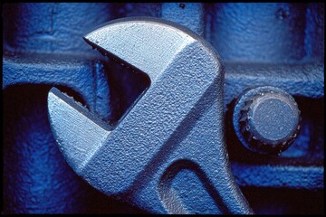 Poster - Close-up view of metallic adjustable wrench resting against blue machinery in a workshop