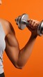 © OleksandrZastrozhnov - Young male holding dumbbell against orange background with visible muscles